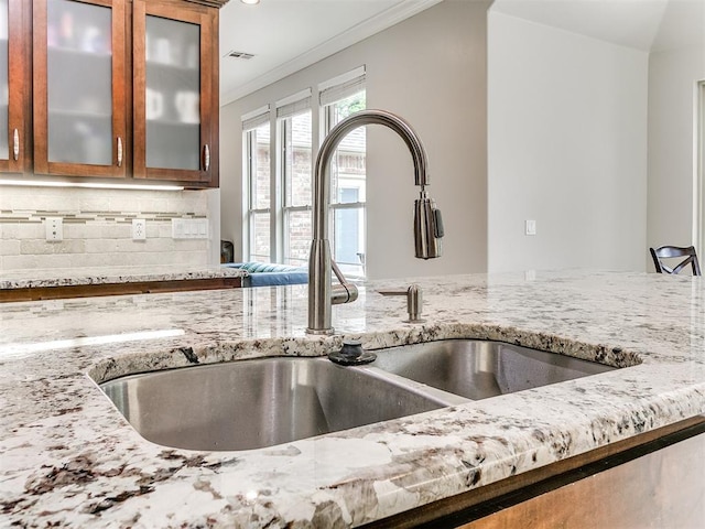 room details with brown cabinets, light stone counters, a sink, decorative backsplash, and ornamental molding
