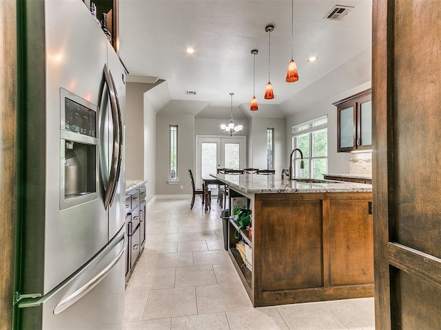 kitchen featuring open shelves, light stone counters, stainless steel fridge, a sink, and visible vents