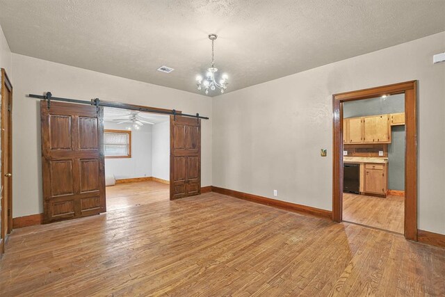 unfurnished room with visible vents, light wood-style floors, baseboards, a barn door, and a chandelier