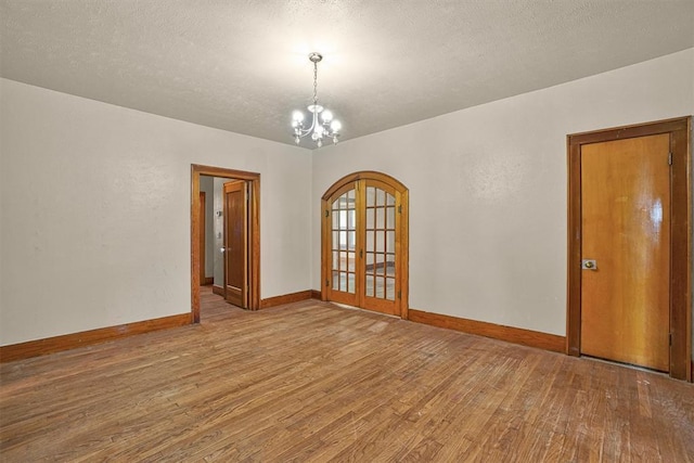 unfurnished room featuring wood finished floors, baseboards, a textured ceiling, a chandelier, and arched walkways