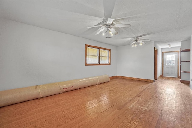 empty room featuring light wood-style floors, baseboards, a ceiling fan, and a textured ceiling