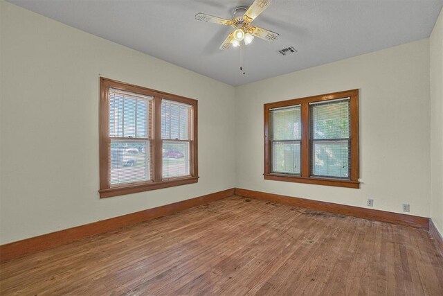 empty room with a ceiling fan, baseboards, visible vents, and wood finished floors