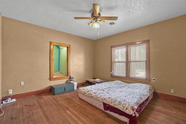 bedroom featuring a textured ceiling, a ceiling fan, baseboards, wood finished floors, and visible vents