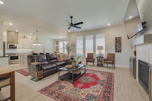 living room featuring recessed lighting, a tiled fireplace, light wood-style flooring, and ceiling fan with notable chandelier
