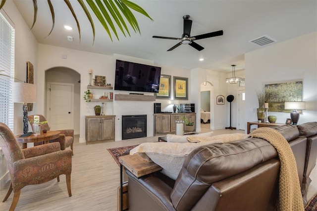 living area featuring ceiling fan, arched walkways, a glass covered fireplace, light wood-style flooring, and visible vents