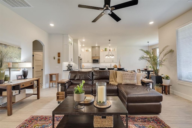 living room featuring arched walkways, ceiling fan with notable chandelier, recessed lighting, light wood-type flooring, and visible vents