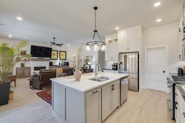 kitchen with ceiling fan, a kitchen island with sink, appliances with stainless steel finishes, a sink, and light wood finished floors