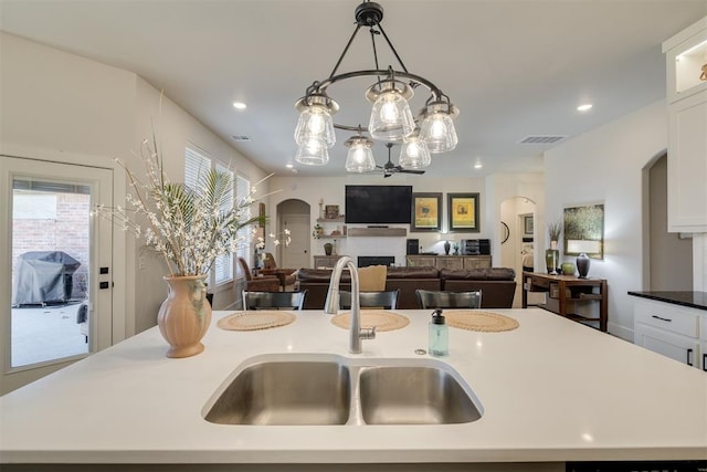 kitchen featuring visible vents, white cabinetry, arched walkways, a sink, and a notable chandelier