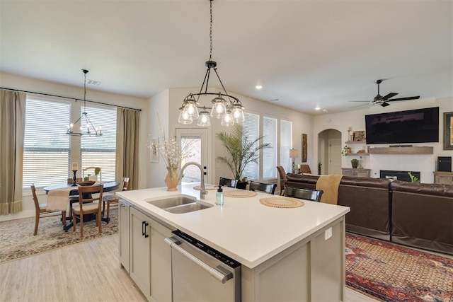kitchen featuring a fireplace, light countertops, a sink, ceiling fan with notable chandelier, and dishwasher