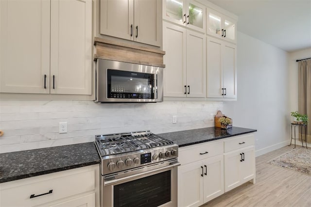 kitchen with light wood-style floors, baseboards, dark stone counters, backsplash, and stainless steel appliances