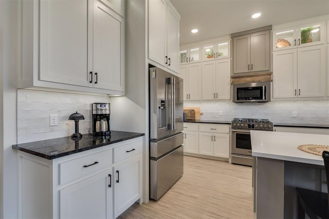 kitchen with glass insert cabinets, appliances with stainless steel finishes, white cabinets, and tasteful backsplash