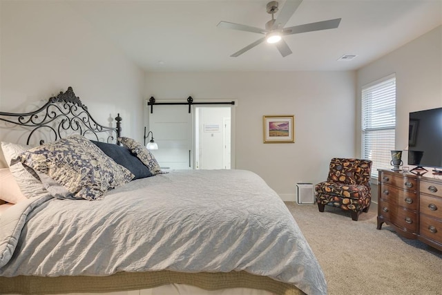 bedroom with visible vents, light carpet, baseboards, ceiling fan, and a barn door