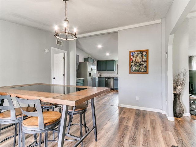 dining area with visible vents, vaulted ceiling, wood finished floors, baseboards, and an inviting chandelier