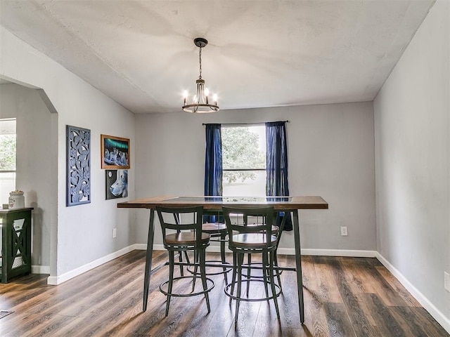 dining room featuring dark wood-style floors, arched walkways, a notable chandelier, and plenty of natural light