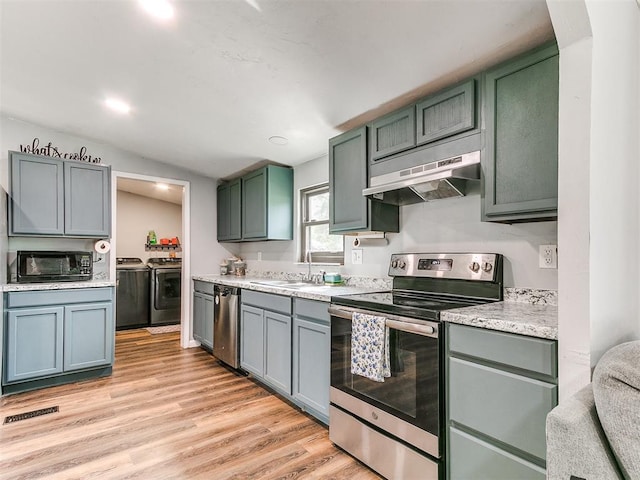 kitchen with light countertops, under cabinet range hood, separate washer and dryer, a sink, and appliances with stainless steel finishes