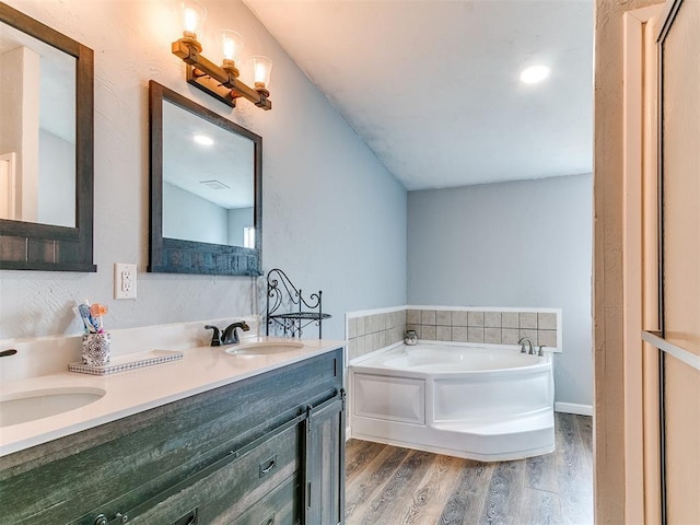 full bath featuring a sink, double vanity, a garden tub, and wood finished floors