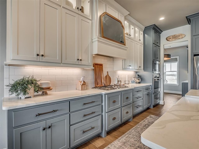 kitchen with light wood-type flooring, appliances with stainless steel finishes, light stone counters, and gray cabinetry