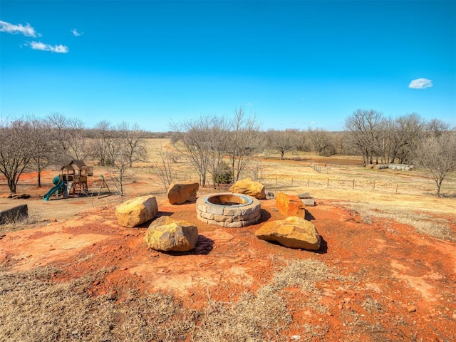 view of yard with a playground, an outdoor fire pit, fence, and a rural view
