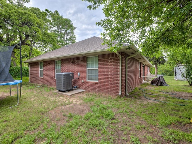 back of house with central air condition unit, a trampoline, a lawn, and brick siding