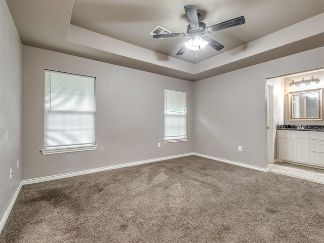unfurnished bedroom featuring a tray ceiling, light colored carpet, baseboards, and visible vents
