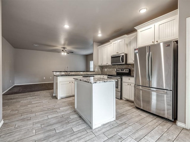 kitchen featuring a peninsula, ceiling fan, appliances with stainless steel finishes, and light wood finished floors