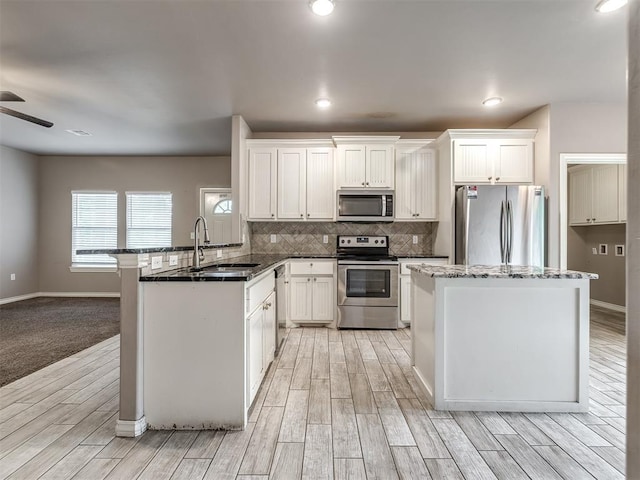 kitchen featuring a ceiling fan, a sink, a peninsula, light wood-style floors, and stainless steel appliances