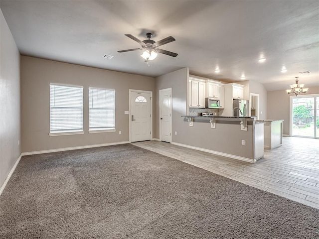 interior space featuring baseboards, open floor plan, a breakfast bar area, white cabinets, and appliances with stainless steel finishes