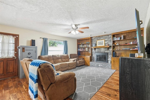 living room with ceiling fan, a textured ceiling, built in features, a brick fireplace, and wood finished floors