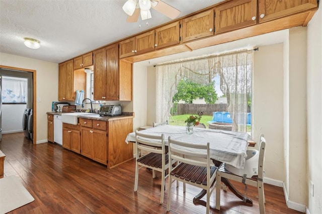 kitchen with brown cabinetry, a ceiling fan, white dishwasher, dark wood-style floors, and a sink