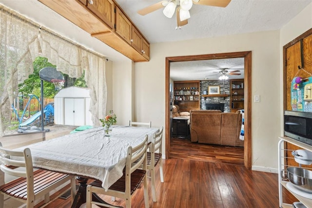 dining room featuring a ceiling fan, a textured ceiling, a fireplace, dark wood finished floors, and baseboards