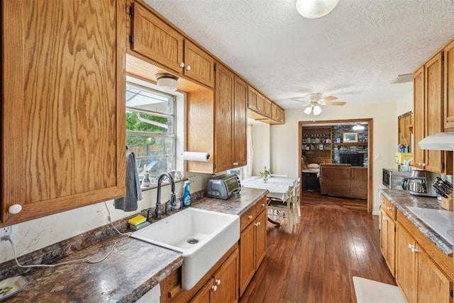 kitchen with ceiling fan, a sink, a textured ceiling, under cabinet range hood, and dark wood-style floors