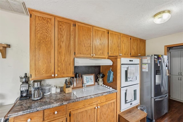 kitchen with brown cabinets, white appliances, a textured ceiling, under cabinet range hood, and visible vents