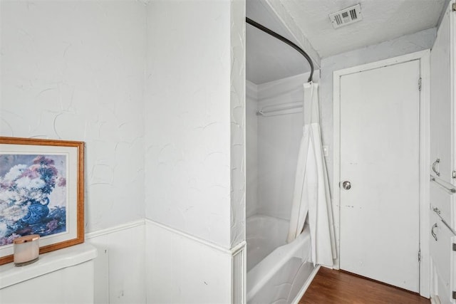 bathroom featuring toilet, shower / bath combo with shower curtain, a wainscoted wall, wood finished floors, and visible vents
