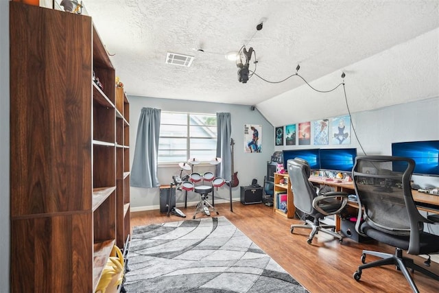 office space featuring a textured ceiling, baseboards, wood finished floors, lofted ceiling, and visible vents