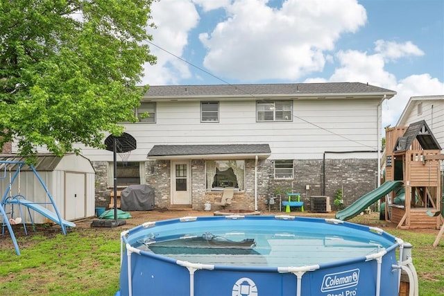 rear view of house featuring an outbuilding, an outdoor pool, brick siding, a shed, and a playground