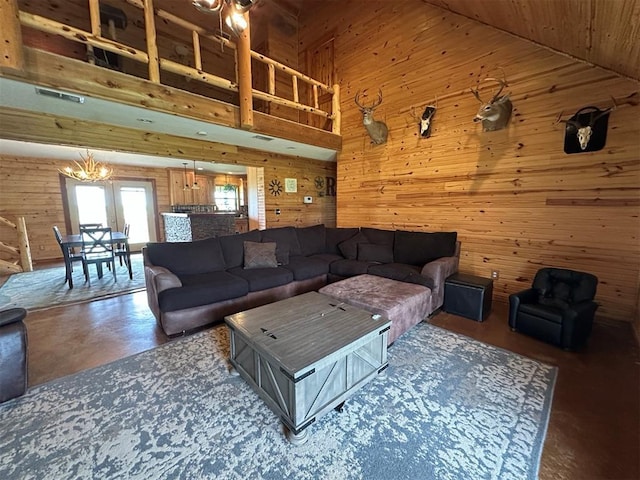 living room with visible vents, concrete flooring, wood walls, high vaulted ceiling, and a notable chandelier