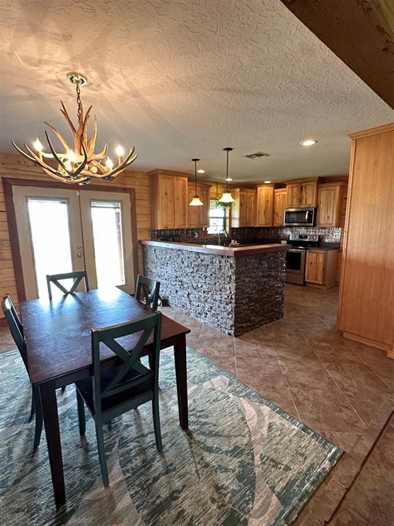 dining room with wooden walls, a textured ceiling, a chandelier, french doors, and visible vents