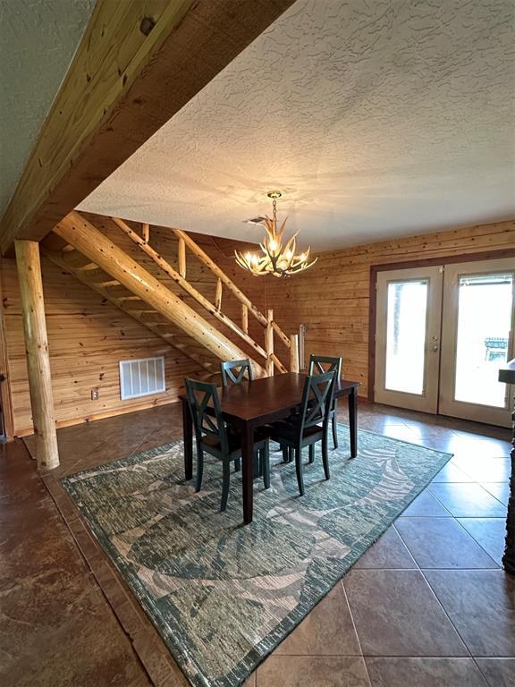 dining room with french doors, wood walls, a textured ceiling, and a chandelier
