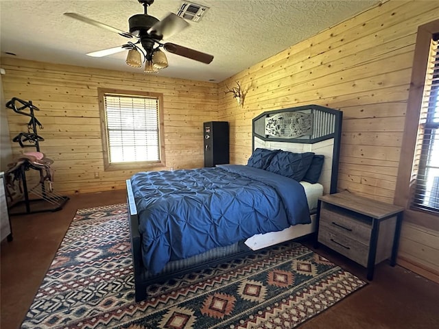 bedroom with wooden walls, a ceiling fan, a textured ceiling, and visible vents