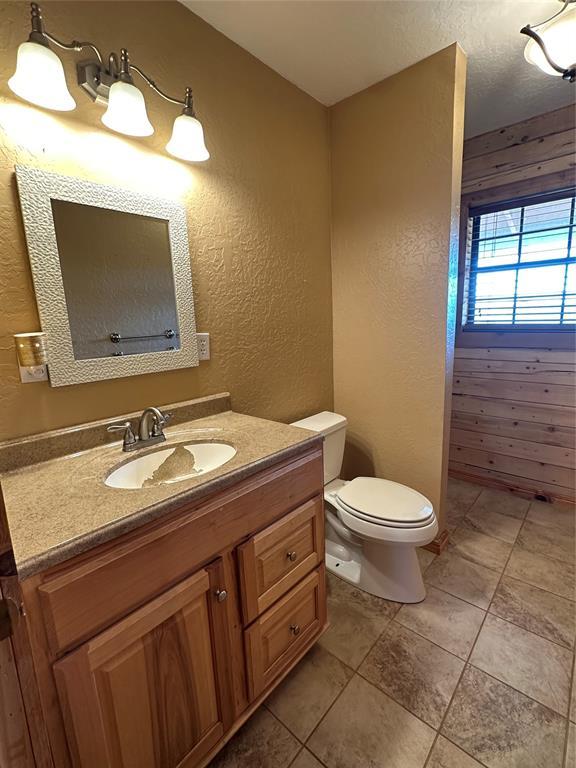 bathroom featuring toilet, a textured wall, tile patterned floors, and vanity
