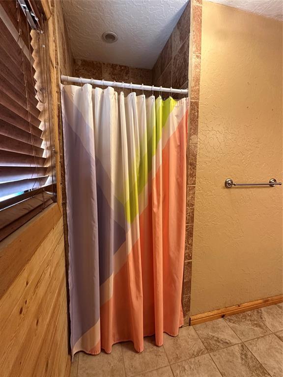 bathroom with baseboards, a textured ceiling, a textured wall, and a shower with curtain