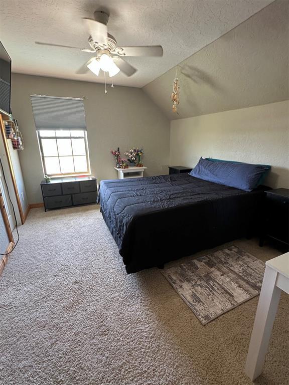 carpeted bedroom with a textured ceiling, vaulted ceiling, and ceiling fan