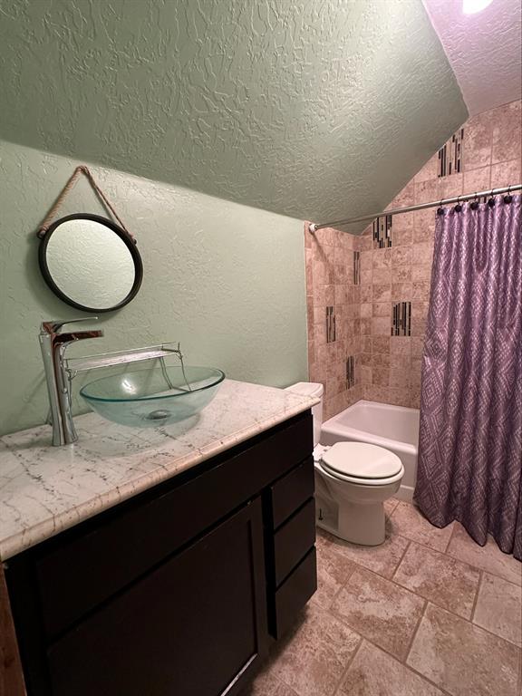 bathroom featuring toilet, a textured wall, lofted ceiling, and shower / tub combo