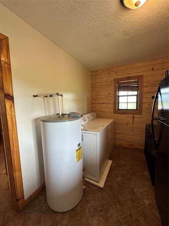 laundry area with laundry area, wood walls, washer / clothes dryer, a textured ceiling, and electric water heater
