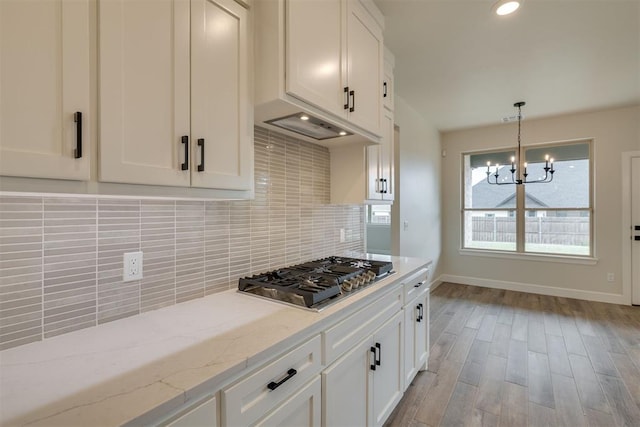 kitchen featuring stainless steel gas cooktop, baseboards, a chandelier, white cabinetry, and decorative backsplash