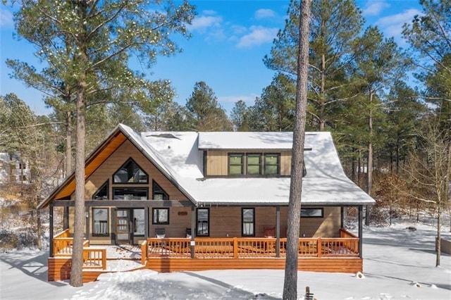 snow covered back of property featuring covered porch