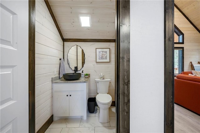 bathroom with toilet, marble finish floor, vanity, vaulted ceiling, and wooden walls