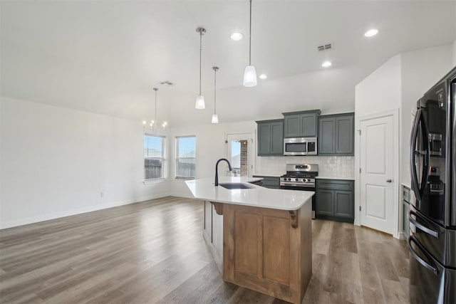 kitchen featuring tasteful backsplash, wood finished floors, a sink, an inviting chandelier, and stainless steel appliances