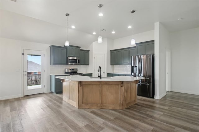 kitchen with appliances with stainless steel finishes, tasteful backsplash, wood finished floors, a sink, and light countertops