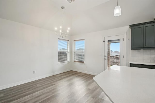 unfurnished dining area featuring vaulted ceiling, a notable chandelier, a healthy amount of sunlight, and light wood finished floors